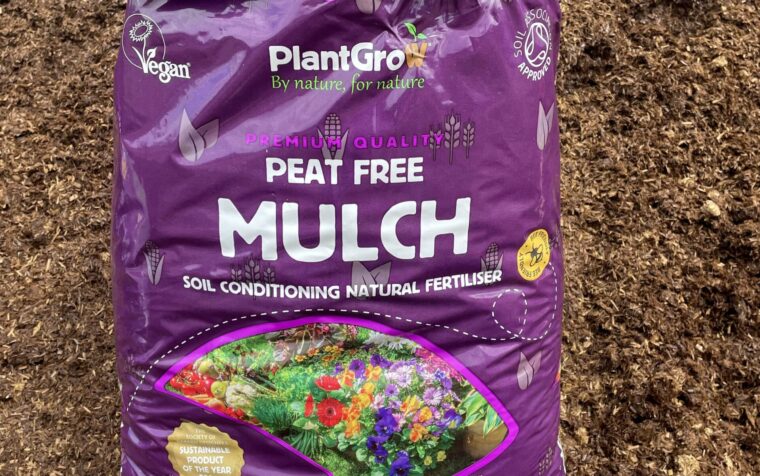 PlantGrow peat-free organic mulch bag displayed on soil, showing purple packaging with vibrant flower imagery and sustainability certifications.