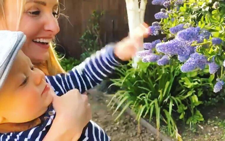 Woman smiling whilst tending vibrant purple flowers in a garden bed, enjoying outdoor gardening and plant care.