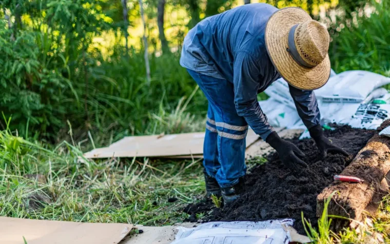 Gardener using no dig method, layering rich compost and soil in raised bed for sustainable vegetable growing.